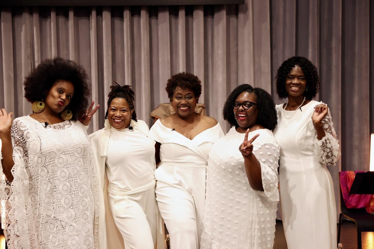Renita Martin with four fellow performers, dressed in white in front of a stage curtain.